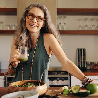 Healthy senior woman smiling while holding some green juice in her kitchen. Mature woman serving herself wholesome vegan food at home. Happy woman taking care of her aging body with a plant-based diet.